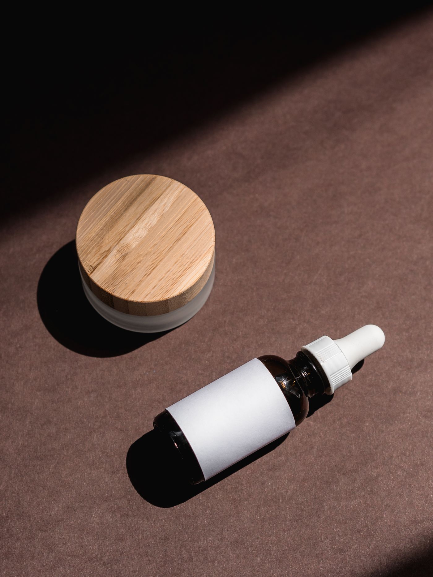 A serum bottle and a small jar arranged on a warm neutral surface