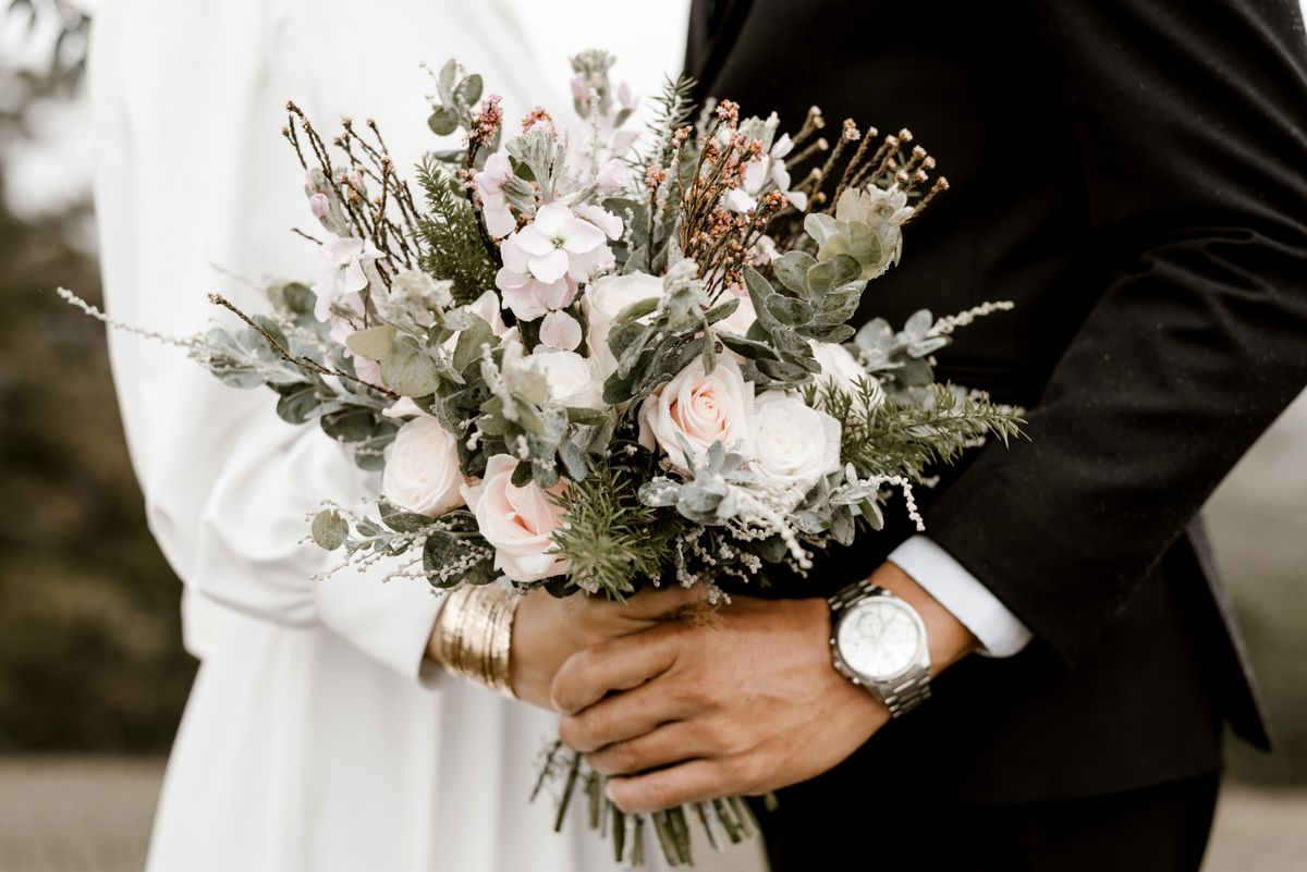 A bride and groom holding a soft winter bouquet